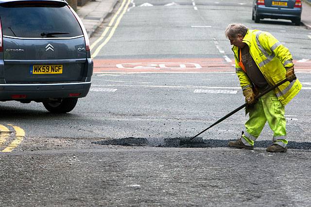 A workman rakes asphalt into a pothole