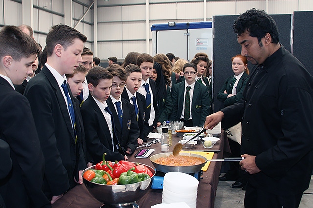 Students watch Councillor Farooq Ahmed holding a cookery demonstration at the Veenas Restaurant stand