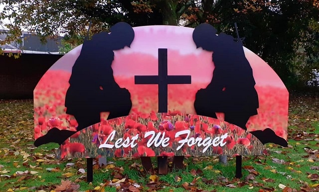 ‘Lest We Forget’, also by Sign & Print, shows two soldiers kneeling by a cross, surrounded by poppies