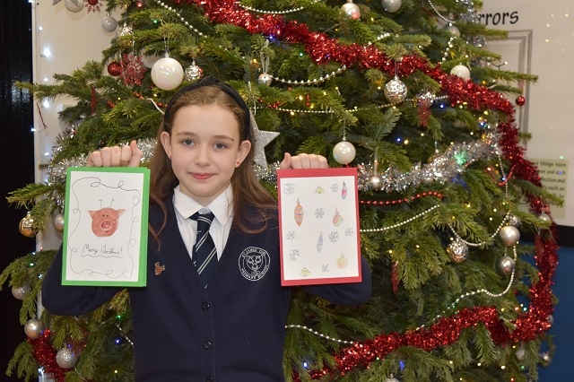 A girl from St James' CofE, Wardle, holds two Christmas cards up in front of a decorated Christmas tree