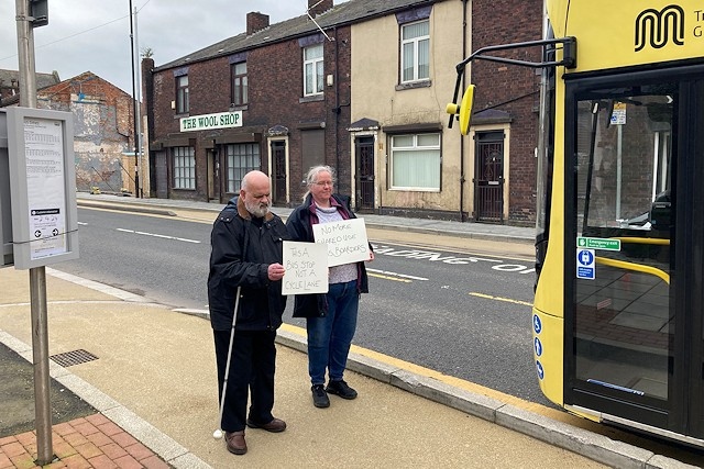 Kevin and Sarah holding up signs as a bus pulls in next to the cycle lane in Castleton
