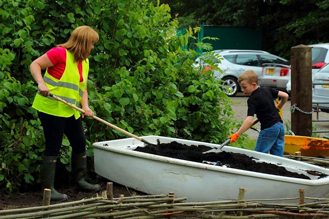 Keeley O'Mara and a young volunteer rake compost in the boat