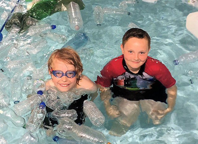 Two children in the pool, surrounded by plastic bottles