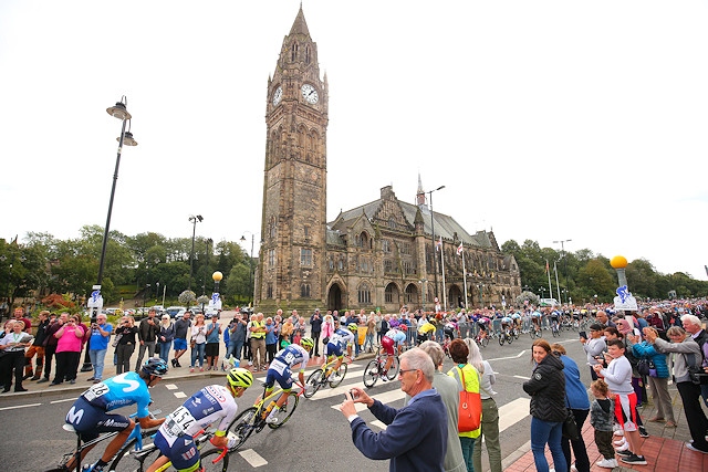 The peloton passes along the Esplanade in front of the town hall