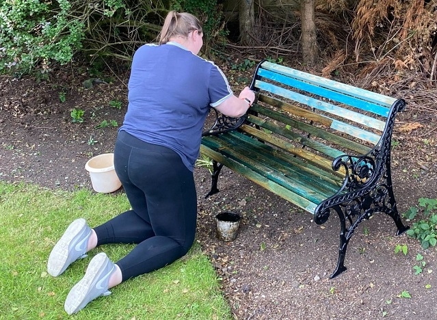A volunteer repairs a bench